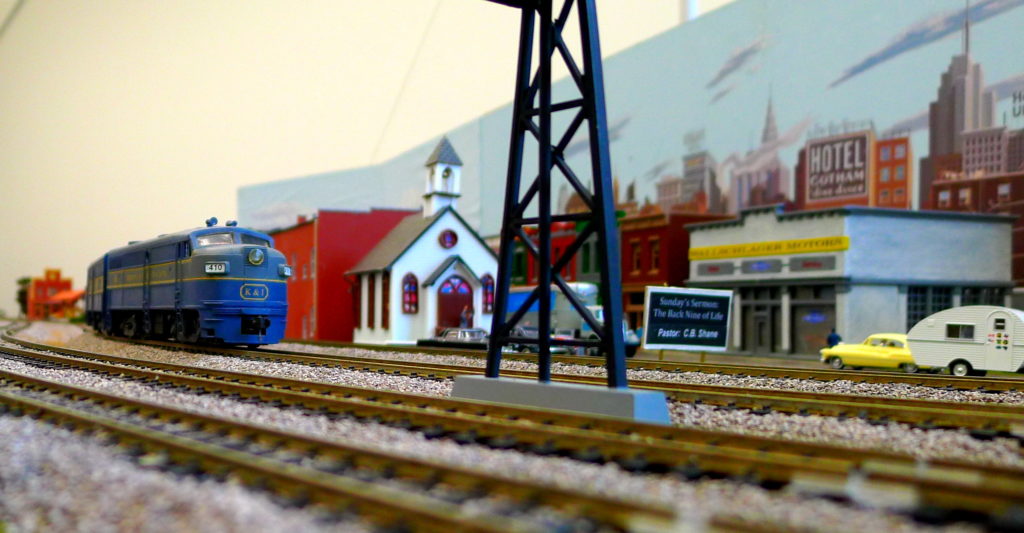 Una foto de un modelo a tren a escala. El tren esta pasando por una ciudad en miniatura.