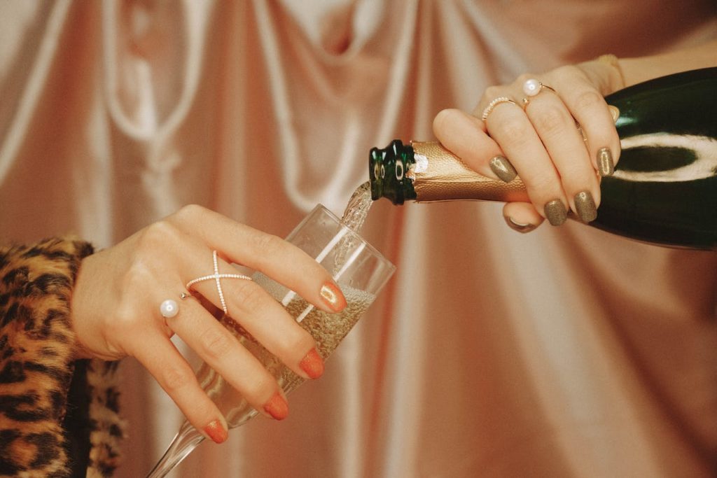 Pantone anuncia El color del año 2024: PEACH FUZZ 6 Una mano sostiene una copa de vido frente a una cortina del color del año 2024, Peach Fuzz